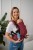 Modelka nosi dziecko w ergonomicznego nosidle KAVKA Multi‑Age burgundy braid cotton - burgundowe nosidło z białym wzorem warkocza  (burgundy carrier with a white braid pattern)